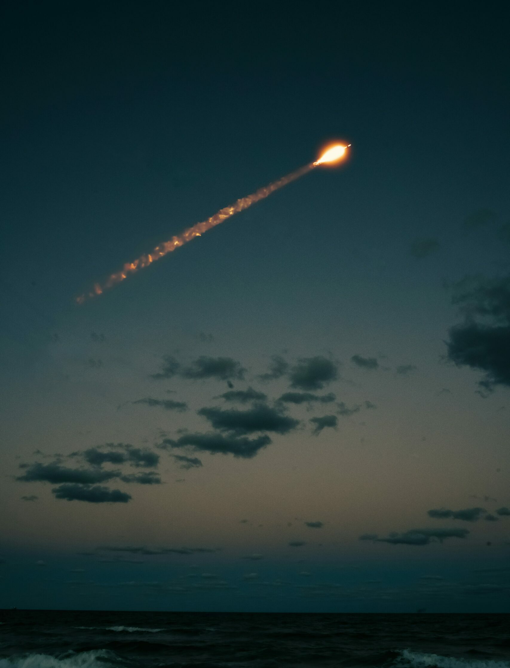 Ciel nocturne au-dessus de l'océan avec un objet lumineux traversant l'atmosphère à grande vitesse, laissant derrière lui une traînée incandescente.