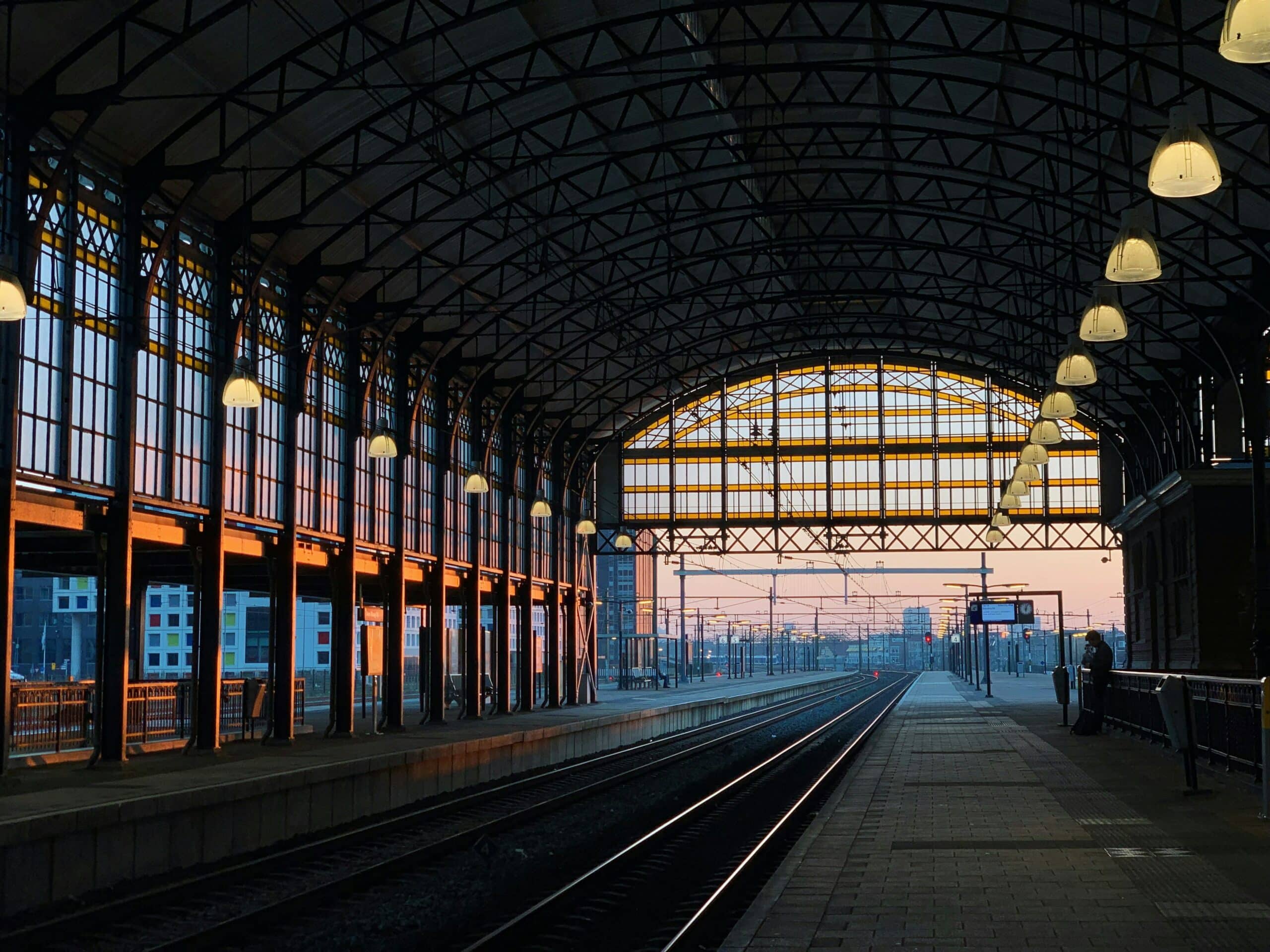Vue perspective des quais d'une gare ferroviaire sous une grande verrière au coucher du soleil, illustrant les enjeux de la géolocalisation indoor en gare
